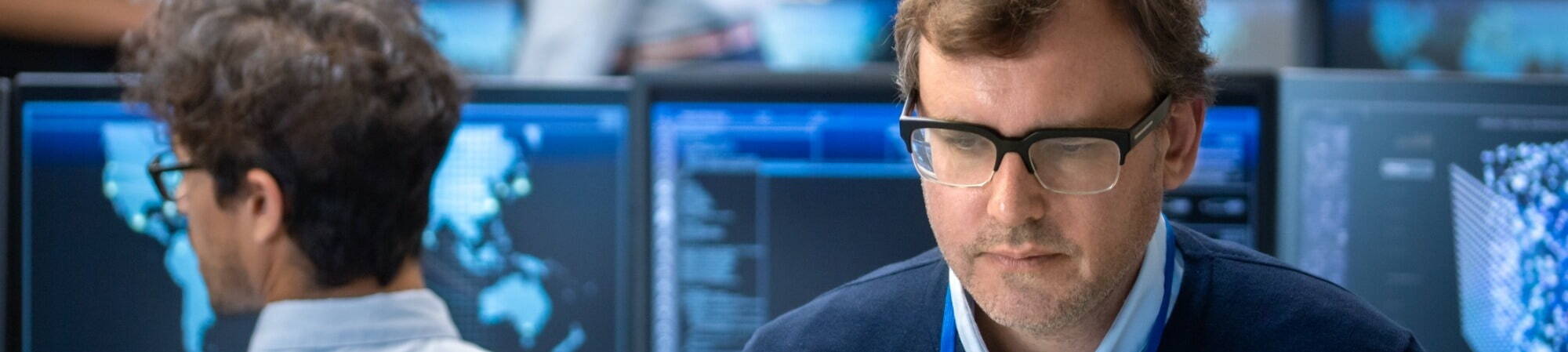 man wearing glasses surrounded by computers