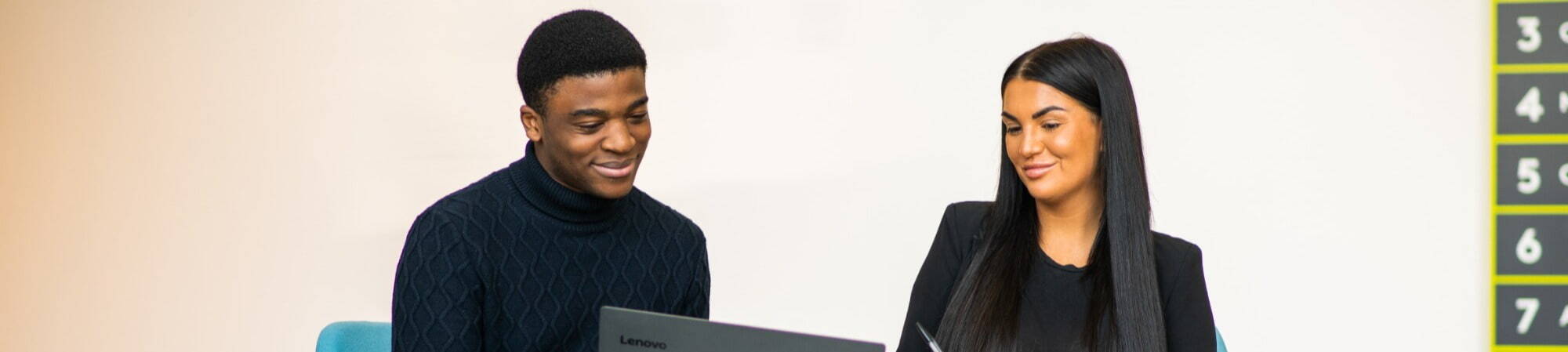 Two people smiling and looking at a laptop whilst conducting a people & culture audit